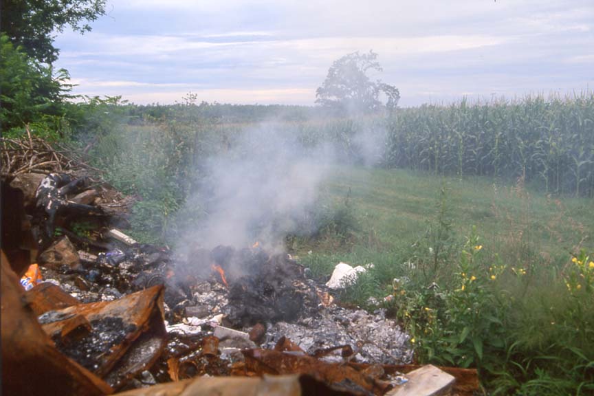 large pile of burning trash beside corn field